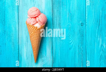 Crème glacée à la framboise dans un cornet de gaufres sur fond bleu. Banque D'Images