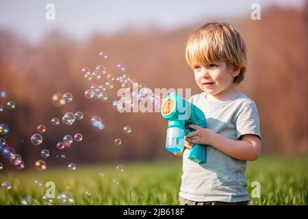 Petit garçon blond jouer savon bulles pistolet stand dans le champ Banque D'Images