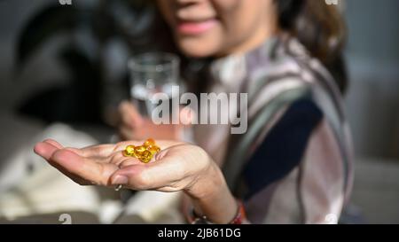 Gros plan, Une pilule de vitamine, des pilules d'huile de poisson omega 3 sur une main de femme âgée avec un arrière-plan flou. Un mode de vie sain et une alimentation saine, des soins de santé. Banque D'Images