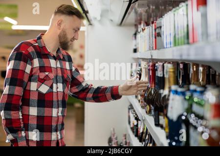 beau shopper masculin en choisissant le champagne au supermarché, un gars debout près de l'étagère avec l'alcool faible du marché du vin, vin mousseux dans l'épicerie Banque D'Images