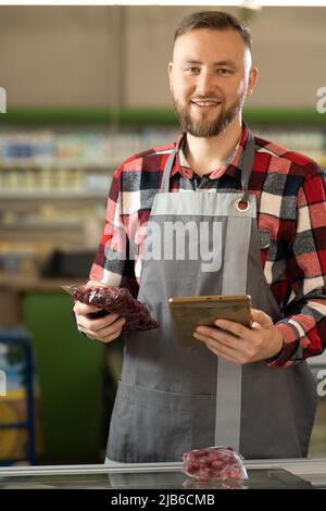 portrait d'un vendeur souriant portant un tablier à l'aide d'une tablette numérique travaillant dans un supermarché Banque D'Images