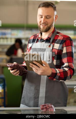 Employé professionnel de supermarché utilisant une tablette à écran tactile et travaillant, souriant à la caméra Banque D'Images