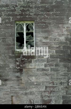 Fenêtre cassée avec verre brisé dans le mur de pierre altérée d'un bâtiment abandonné Banque D'Images
