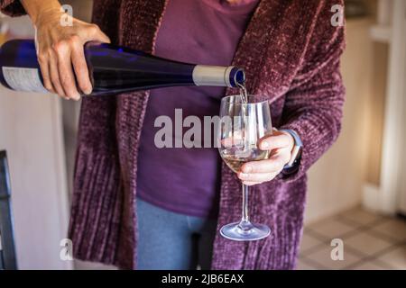 Une femme en hiver verse un verre de vin blanc Banque D'Images