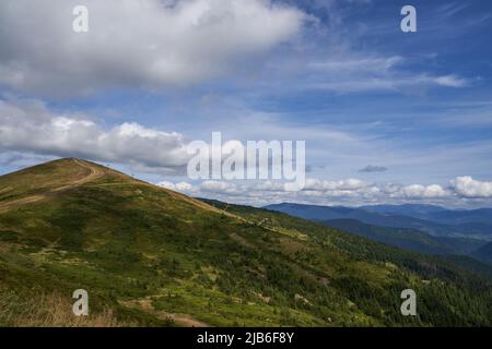 Vue panoramique sur la douce pente de la montagne, avec le chemin menant au sommet de la colline en été. Les nuages Cumulus, traversant le ciel bleu, semblaient toucher le sommet du mont, avec un paysage vallonné sur fond. Concept de haute terre. Banque D'Images