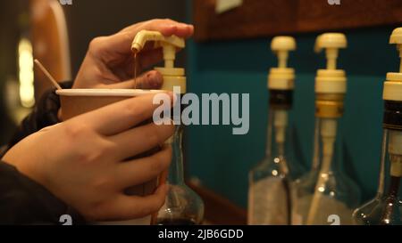 Les femmes ajoutent du sirop à la main dans la ciffee. Du sirop de noisette pour le café. Les noix dans le café comme le sirop. Café avec sirop Banque D'Images