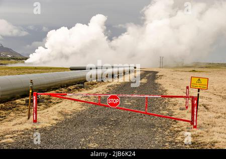 Hengill, Islande, 22 avril 2022: Clôture, route, Pipeline, vapeur chaude et panneau de danger à la centrale géothermique de Hellisheiði Banque D'Images