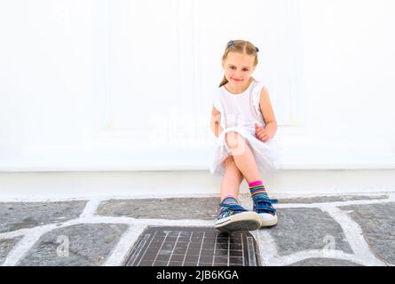 Petite jolie fille blong dans une robe blanche assise à l'extérieur Banque D'Images