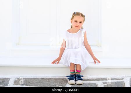 Petite jolie fille blong dans une robe blanche assise à l'extérieur Banque D'Images