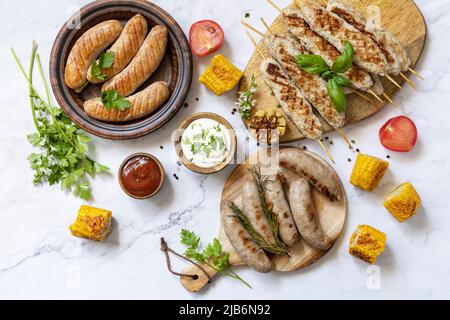 Repas de fête d'été. Menu de grillades. Diverses saucisses grillées au barbecue avec des herbes fraîches et des épices sur une table en marbre. Vue de dessus. Banque D'Images