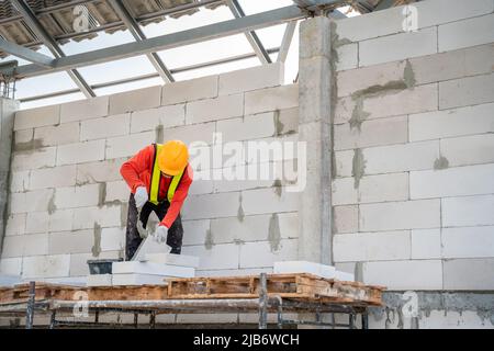 Un travailleur de la construction utilise du mortier adhésif pour les briqueteries légères sur le chantier de construction. Banque D'Images