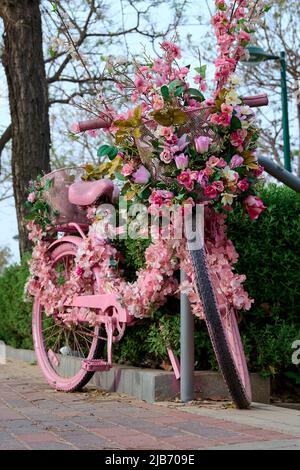 un vélo rose décoré de fleurs est laissé dans la rue en gros plan. Banque D'Images