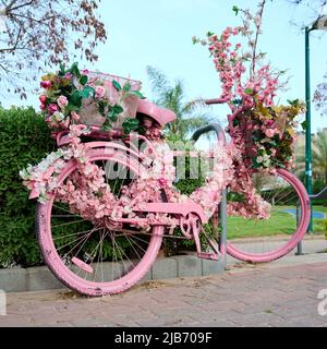 un vélo rose décoré de fleurs est laissé dans la rue en gros plan. Banque D'Images