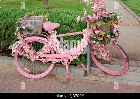 un vélo rose décoré de fleurs est laissé dans la rue en gros plan. Banque D'Images