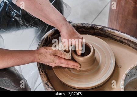 Mains de la femme âgée sculptant vase en argile sur la roue de potter. Banque D'Images
