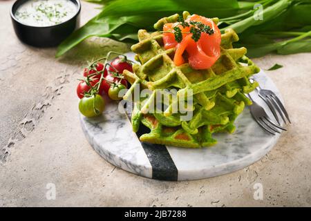 Gaufres belges vertes. Épinards ou ail sauvage ou gaufres au pesto avec saumon rouge et sauce à la crème sur fond de table en béton gris. Délicieux petit déjeuner, Banque D'Images