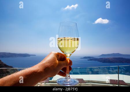 Un verre de vin blanc à la main sur la toile de fond de la mer Égée et de la caldeira sur l'île de Santorini Banque D'Images