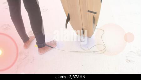 Image de taches de lumière colorées sur les pieds du surfeur sur la plage tenant la planche de surf Banque D'Images