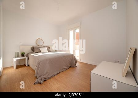 Chambre avec lit double avec miroir rond, couvre-lit gris et accès à une terrasse Banque D'Images