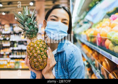 Portrait bonne jolie fille portant un masque de protection tenant l'ananas dans un supermarché pendant le shopping d'épicerie Banque D'Images