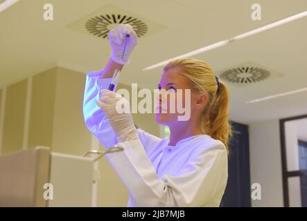 Une jeune étudiante prend ses fonctions d'assistante de laboratoire. Elle porte une blouse médicale blanche. Elle est vue analyser et faire des recherches sur son lieu de travail. Banque D'Images