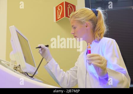 Une jeune étudiante prend ses fonctions d'assistante de laboratoire. Elle porte une blouse médicale blanche. Elle est vue analyser et faire des recherches sur son lieu de travail. Banque D'Images