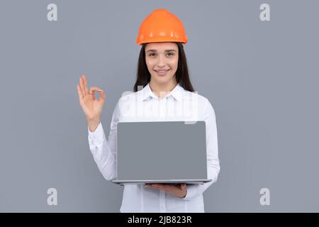 Jeune femme responsable de la construction. Femme constructeur portrait isolé avec casque de protection et ordinateur portable. Arrière-plan gris, espace de copie. Banque D'Images