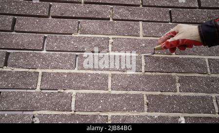 Un travailleur applique du mortier à la façade d'un bâtiment. Carreaux de ciment sur la façade du bâtiment. Carreaux de ciment dans la rue. Banque D'Images