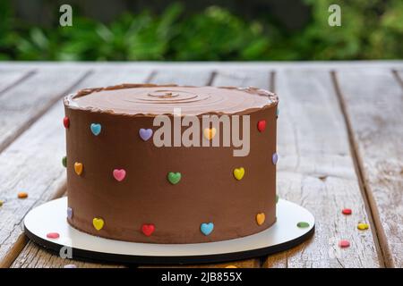 Gros plan de gâteau au chocolat recouvert de ganache au chocolat semisweet. Jardin en arrière-plan. Banque D'Images