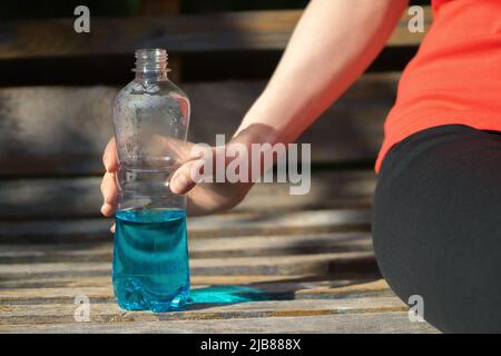 La fille se repose sur un banc de parc tenant une boisson isotonique bleue dans sa main. Banque D'Images