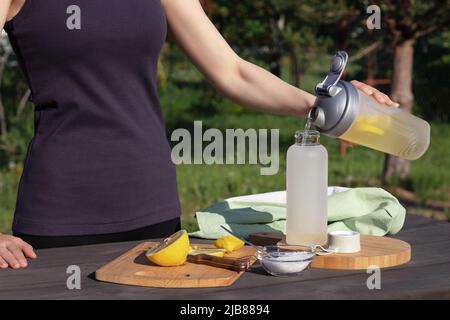 Une jeune fille prépare une boisson isotonique maison fraîche à partir d'ingrédients naturels - sel, citron et eau minérale. Banque D'Images