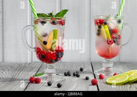 Cocktails d'été frais faits maison avec glace, citron vert et baies dans des verres avec une paille Banque D'Images