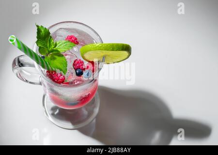 Cocktail d'été rafraîchissant avec glace, lime et baies dans un verre avec une paille, copyspace. Banque D'Images