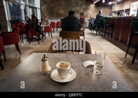 Photo d'une photo macro d'une tasse de café utilisée pour l'espresso, vide, sale et tachée, sur une table noire d'un café bar avec un verre plein d'eau à l'arrière Banque D'Images