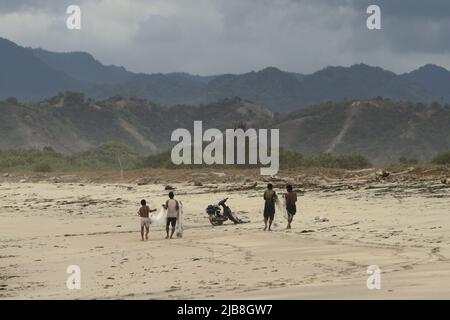 Pêcheurs portant des filets de pêche lorsqu'ils marchent sur la plage de Kalala par une journée nuageuse à Wula, Wula Waijelu, East Sumba, East Nusa Tenggara, Indonésie. Banque D'Images