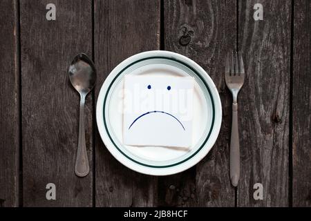 triste udibka dessiné sur un morceau de papier se trouve sur une assiette vide sur la table, tristesse quand il n'y a rien à manger, faim et mauvaise humeur Banque D'Images