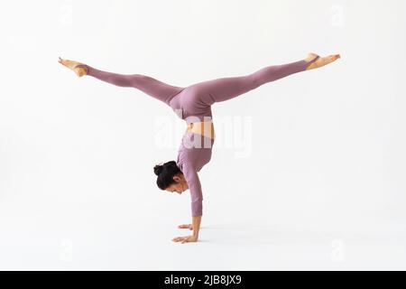 Une femme pratiquant le yoga exécute l'exercice Adho Mukha Vrikshasana avec Samakonasana, une main avec des fentes longitudinales sur un fond blanc Banque D'Images