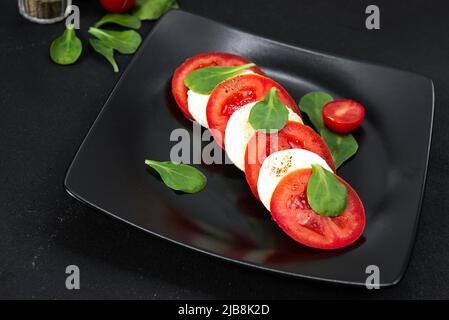 Salade italienne sur une assiette noire avec fromage et tomates. Cuisine européenne Banque D'Images