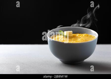 La polenta est un plat traditionnel italien. Plaque grise avec polenta de porridge de maïs avec un morceau d'huile sur un fond gris vient la vapeur de la cuit Banque D'Images