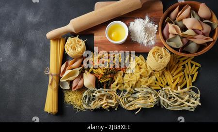 Assortiment de pâtes brutes. Différents types de macaroni, tagliatelle, farfalle, spaghetti, penne rigate . Coloré, rouge, vert, jaune, nouilles. Banque D'Images