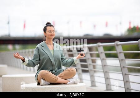 Photo d'une femme médite sur le remblai. Elle est à l'abri de l'agitation des bureaux et du bruit de la ville. Concept de détox numérique. Banque D'Images