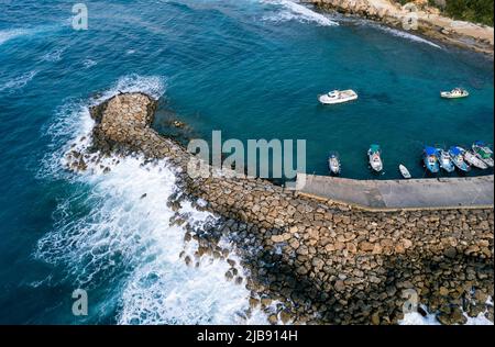 Vue aérienne par drone des bateaux de pêche amarrés au port au brise-lames. Vagues de tempête en mer Banque D'Images