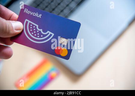 Main humaine tenant une carte de débit Revolut. Paiement numérique de l'application de téléphone mobile en ligne avec un ordinateur portable Banque D'Images