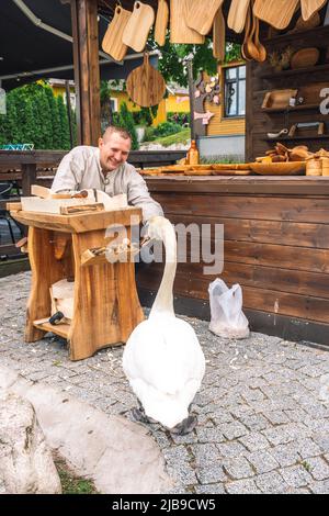 Un artisan lituanien en costumes traditionnels sculptant du bois et vendant ses objets et objets en bois faits main sur un marché de rue local à Trakai Banque D'Images