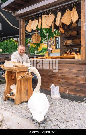 Un artisan lituanien en costumes traditionnels sculptant du bois et vendant ses objets et objets en bois faits main sur un marché de rue local à Trakai Banque D'Images