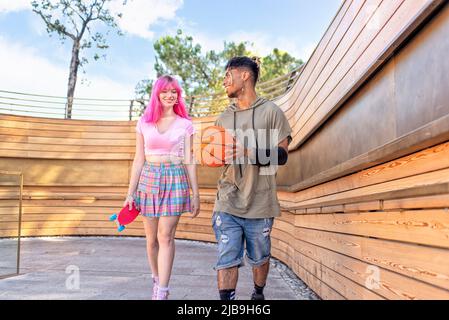 autre couple varié qui se tient ensemble pour se détendre et se promener dans la ville. heureux amis interraciaux tenant le skateboard et le basket-ball Banque D'Images