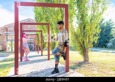 autre couple divers traînant ensemble dans un parc tenant un smartphone en ligne sur les médias sociaux web regarder la vidéo. interracial adolescents amis Banque D'Images