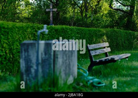 09 mai 2022, Basse-Saxe, Brunswick : un point d'écoulement de l'eau se trouve à côté d'un banc en bois devant une grande croix dans le cimetière du district de Watenbüttel. Photo: Stefan Jaitner/dpa Banque D'Images