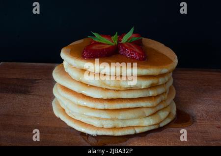 Crêpes aux fraises fraîches, à la menthe et au sirop sur une assiette en bois. Isolé sur fond sombre, concentré sélectif, en-cas de petit-déjeuner américain. Banque D'Images