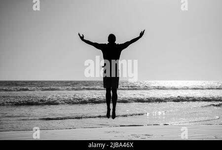 silhouette d'homme sportif sautant avec les mains levées sur la plage d'été, la liberté Banque D'Images